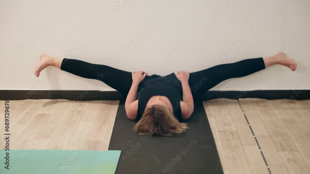 Woman with split legs stretching against wall. Healthy female is practicing yoga on mat at studio. She is wearing active wear at healthcare center. Woman with split legs stretching against wall. Healthy female is practicing yoga on mat at studio. She is wearing active wear at healthcare center.