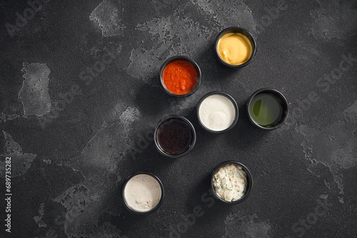 A variety of dipping sauces presented in black ramekins against a textured dark backdrop, perfect for culinary accents