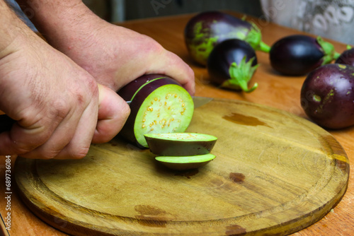 Close-up view of male hands cutting eggplant on chopping board in kitchen