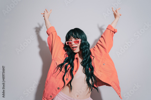 Cheeky emotional fashion young woman with long green color hair and trendy peach color lips, jacket and sunglasses dances on white background. Playful Hipster woman having fun. Color of the 2024 year. photo