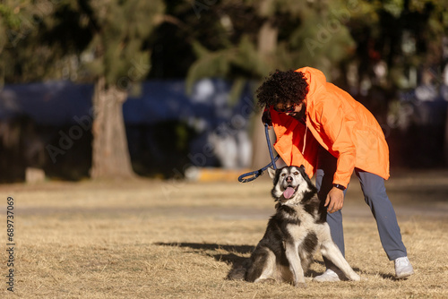 Young Mexican man with curly hair, petting with a husky dog in a park