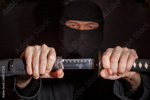 Ninja ready to fight, holding a Japanese sword. Photo of a warrior dressed in black clothes and closed face