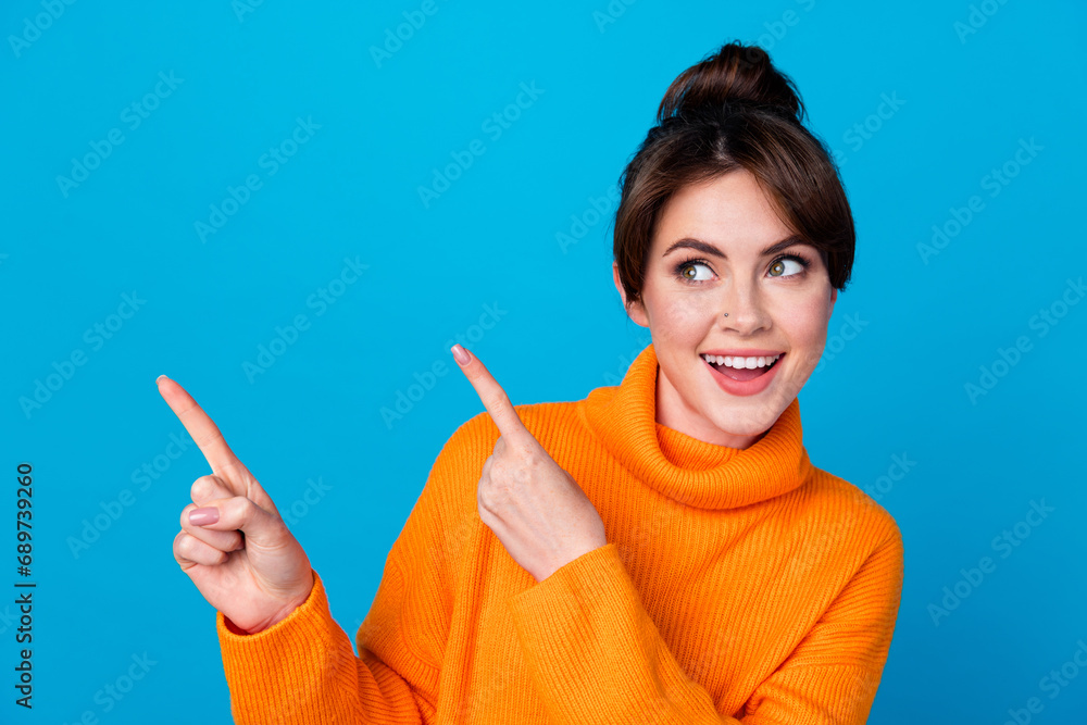 Photo of excited funky lady wear knitted pullover pointing two fingers looking empty space isolated blue color background Photo of excited funky lady wear knitted pullover pointing two fingers looking empty space isolated blue color background