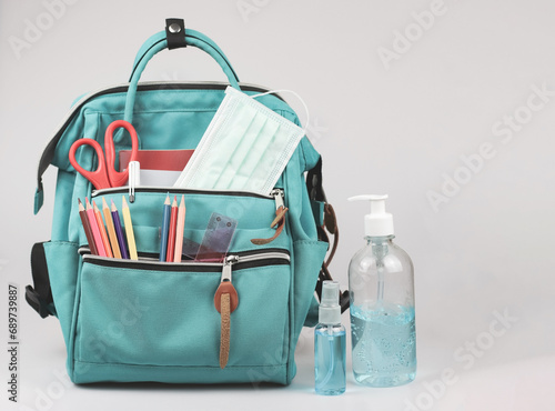 backpack with school supplies , medical mask and alcohol sanitizer gel on white background with copy space. COVID-19 prevention while going back to school and new normal concept.