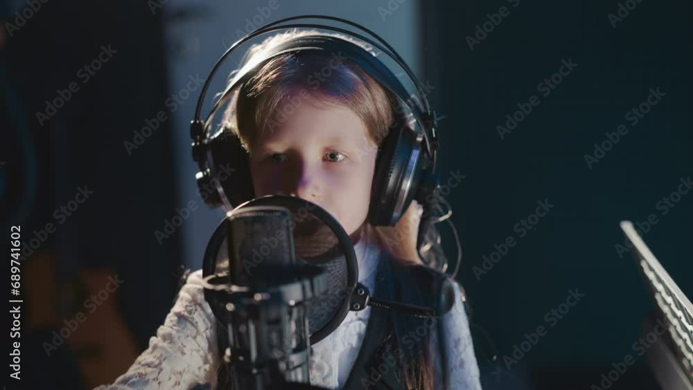 Young singer gestures while performing closeup. Child captures rhythm while laying down track in recording studio. Recording session with small girl Young singer gestures while performing closeup. Child captures rhythm while laying down track in recording studio. Recording session with small girl