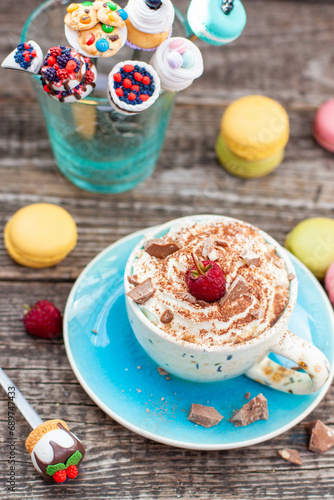 A beautiful blue cup of coffee with whipped cream, cocoa powder and raspberries on rustic wooden background
