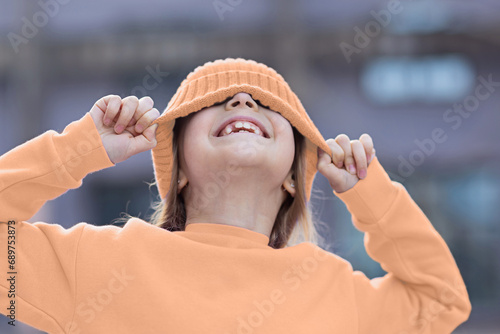 Trendy color of the 2024 year peach fuzz. Cute little caucasian girl eight years old with blonde hair smiling outdoor. Kid wearing stylish shirt and knitted hat photo