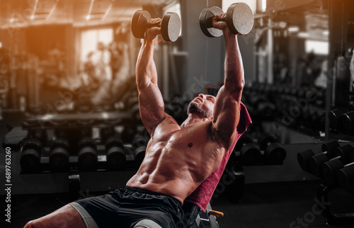 Muscular man doing bench press with heavy dumbbells for chest workout