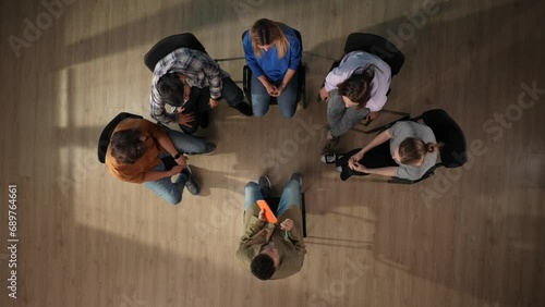 In the shot above, a group of people are sitting in a therapy session. Across from them sits a doctor psychiatrist, chatting with them, listening. Then one man freaks out and leaves. Top view photo
