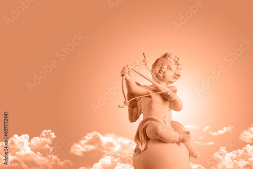Color of the year 2024, Peachy Fuzz, Figurine of an angel Cupid on the podium with a bow and arrow on a blu sky with clouds background . Valentine's Day.