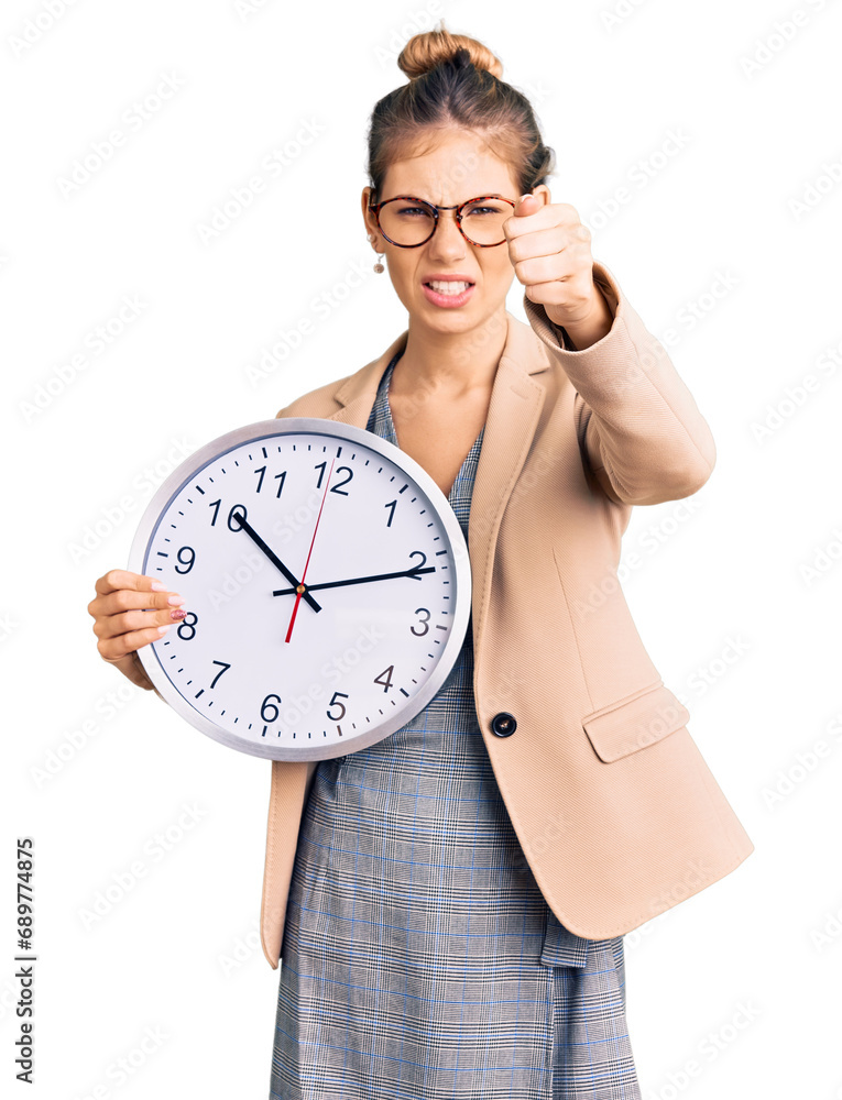 Beautiful caucasian woman with blonde hair wearing business jacket and holding clock annoyed and frustrated shouting with anger, yelling crazy with anger and hand raised Beautiful caucasian woman with blonde hair wearing business jacket and holding clock annoyed and frustrated shouting with anger, yelling crazy with anger and hand raised