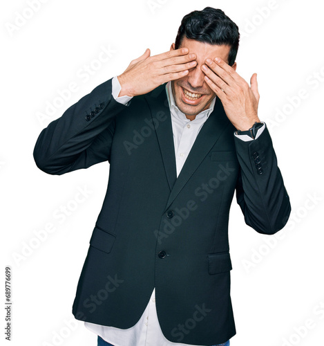 Handsome hispanic man wearing business clothes covering eyes with hands smiling cheerful and funny. blind concept.