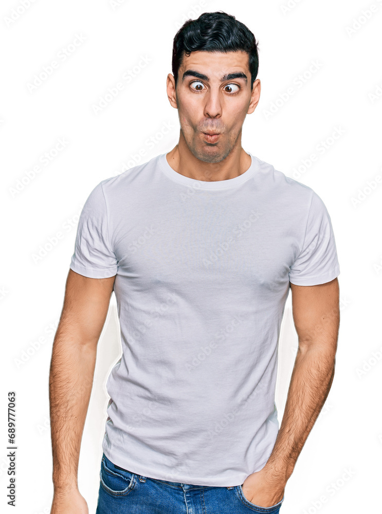 Handsome hispanic man wearing casual white t shirt making fish face with lips, crazy and comical gesture. funny expression. Handsome hispanic man wearing casual white t shirt making fish face with lips, crazy and comical gesture. funny expression.