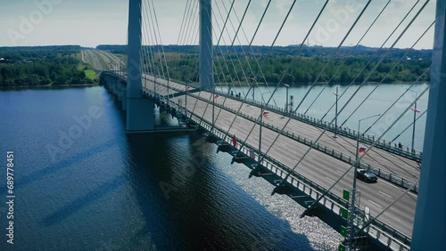 A vintage car with no roof rides over a new modern suspension bridge. Six-lane highway, new markings, guardrails on the side of the road. Drone shot photo