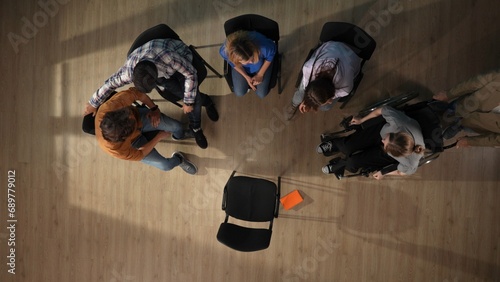 In the shot above a group of people, male and female, are sitting on a chair. They have come to a meeting, a session, therapy. They are discussing something, talking, smiling, waiting for a mentor