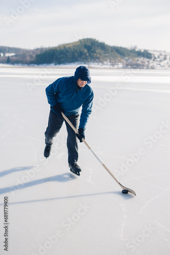 Photography Senior man playing hockey on a frozen lake in winter.