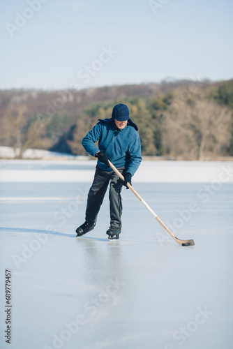 An elderly man practices ice hockey on a frozen lake in winter.