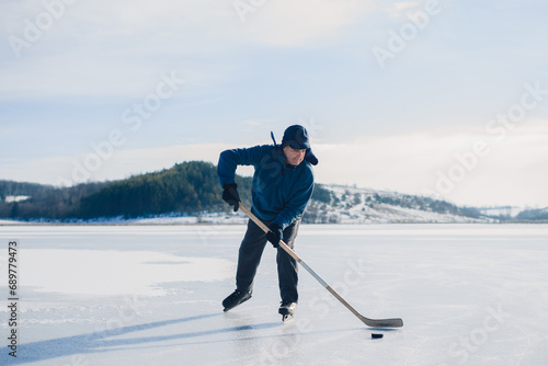 An elderly man practices stricking the puck with hockey sticks on a frozen lake in winter.