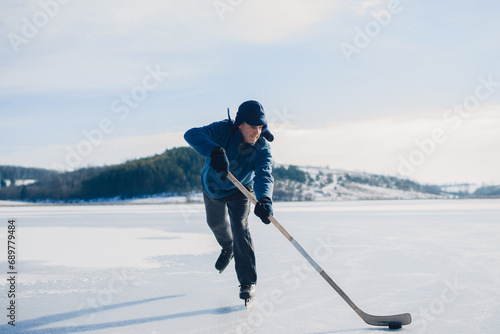 An elderly man practices stricking the puck with hockey sticks on a frozen lake in winter.
