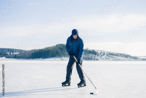 An elderly man practices stricking the puck with hockey stick on a frozen lake in winter. photo