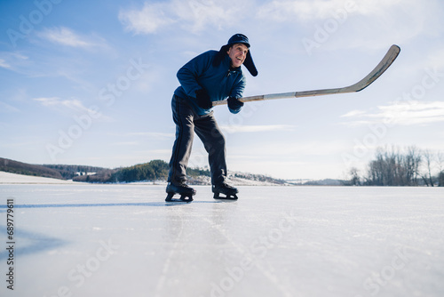 Canvas Print An elderly man practices stricking the puck with hockey stick on a frozen lake in winter
