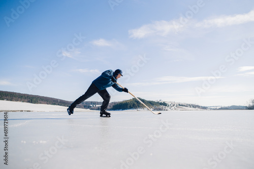 An elderly man practices stricking the puck with hockey stick on a frozen lake in winter. © dsheremeta