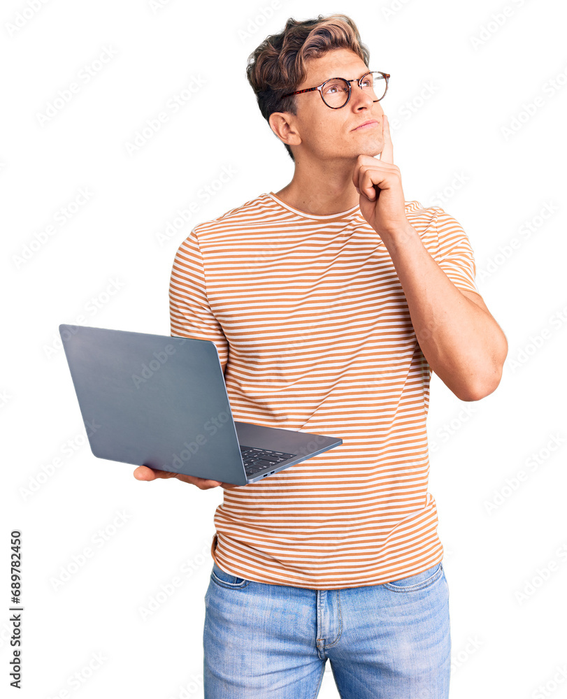 © Krakenimages.com - Young handsome man wearing glasses holding laptop serious face thinking about question with hand on chin, thoughtful about confusing idea