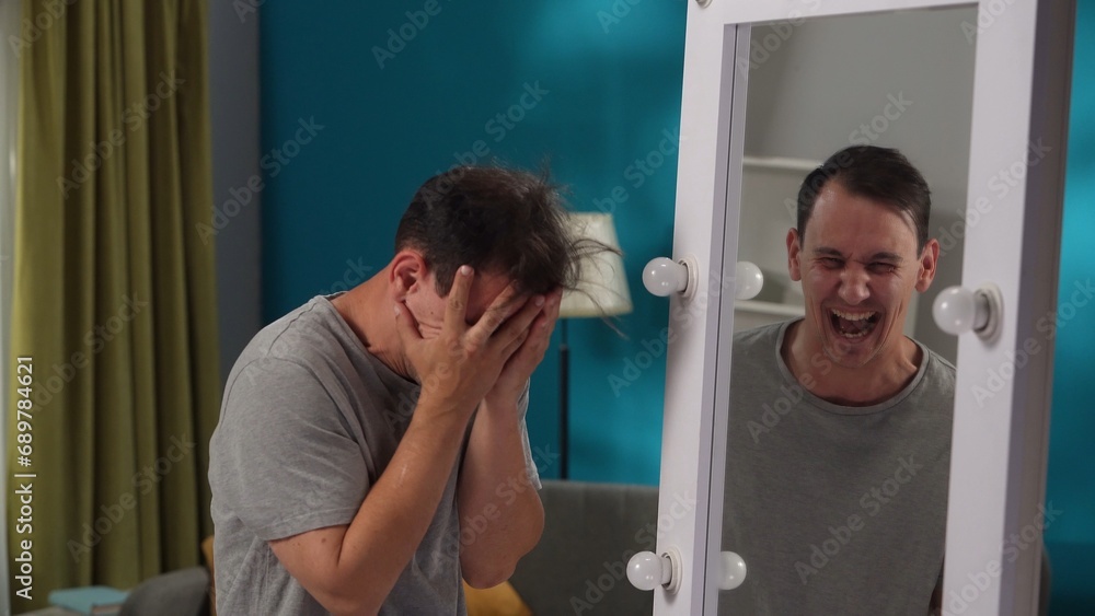 A man suffering from a mental disorder stands in front of a mirror, hiding his face in his hands, close up. Apathy, inner conflict, psychological problems. A man suffering from a mental disorder stands in front of a mirror, hiding his face in his hands, close up. Apathy, inner conflict, psychological problems.