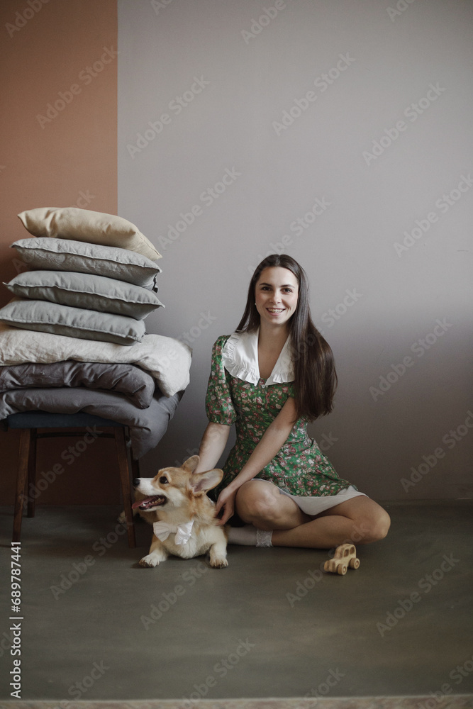 Woman with corgi sitting near pile of pillows in the bedroom. Woman portrait