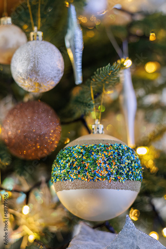 Festive glass balls with colored sparkles, Christmas tree and yellow bokeh of glowing garland.