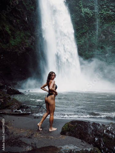 Gorgeous young woman in bikini posing near waterfall in Bali.