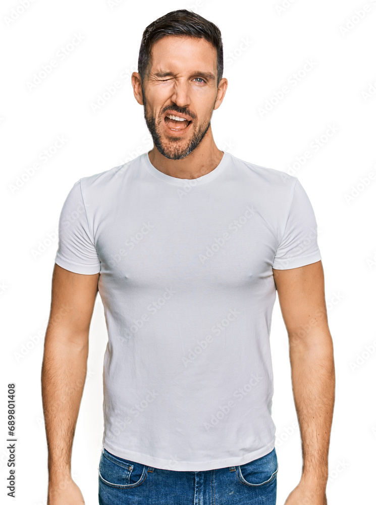 Handsome man with beard wearing casual white t shirt winking looking at the camera with sexy expression, cheerful and happy face. Handsome man with beard wearing casual white t shirt winking looking at the camera with sexy expression, cheerful and happy face.