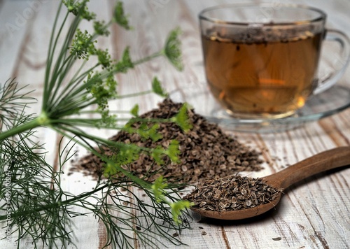 Medicinal tea with dried dill seeds in a cup and a pile of seeds on a natural wooden table. The concept of the usefulness of dill.