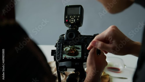 Close up shot of hands of female photographer and food stylist discussing image on viewfinder of professional digital camera while taking food photos in studio photo