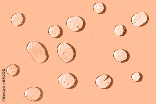 Cosmetic hydrating product or ingredient concept. Peach fuzz color drops of transparent liquid on a trendy color background. Drops gel or oil close up.