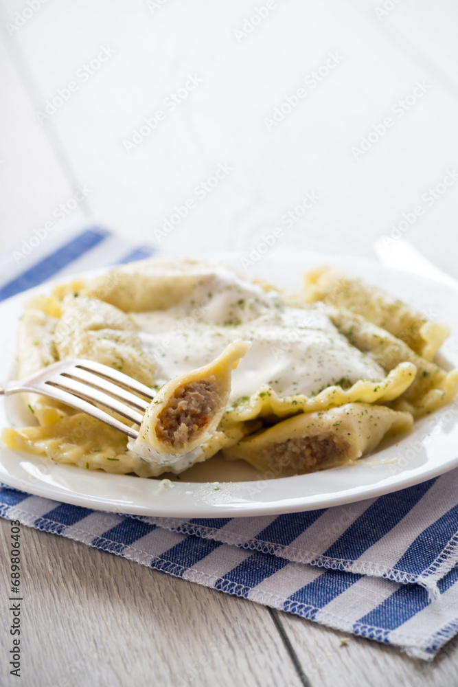 cooked dumplings with meat, spices and sour cream, in a plate on a light wooden table. cooked dumplings with meat, spices and sour cream, in a plate on a light wooden table.