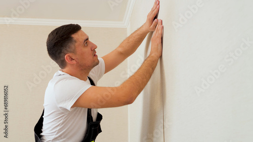 Professional Caucasian worker glues a strip of wallpaper on the wall. Man with dark hair in a uniform glueing wallpaper.