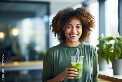 A beautiful African American woman is smiling and drinking a detox cocktail at home in the kitchen photo