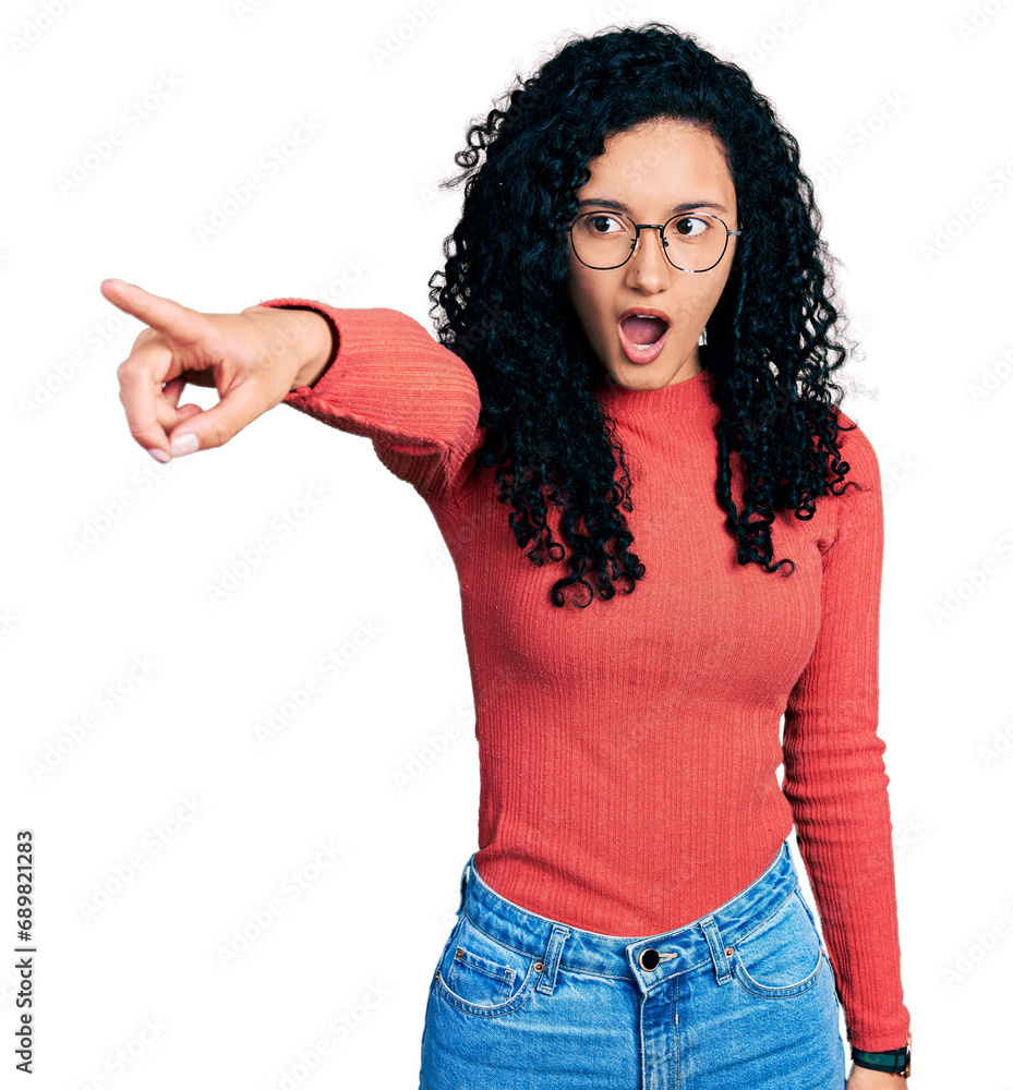 Young hispanic woman with curly hair wearing glasses pointing with finger surprised ahead, open mouth amazed expression, something on the front Young hispanic woman with curly hair wearing glasses pointing with finger surprised ahead, open mouth amazed expression, something on the front