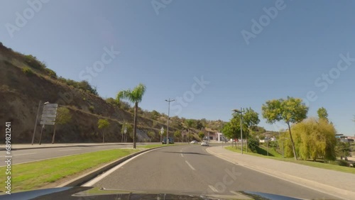 First person view, FPV, from dashcam of car driving along the Algarve Coast in Portugal in Albufeira, driving in the city. Road trip video in POV, with blue sky