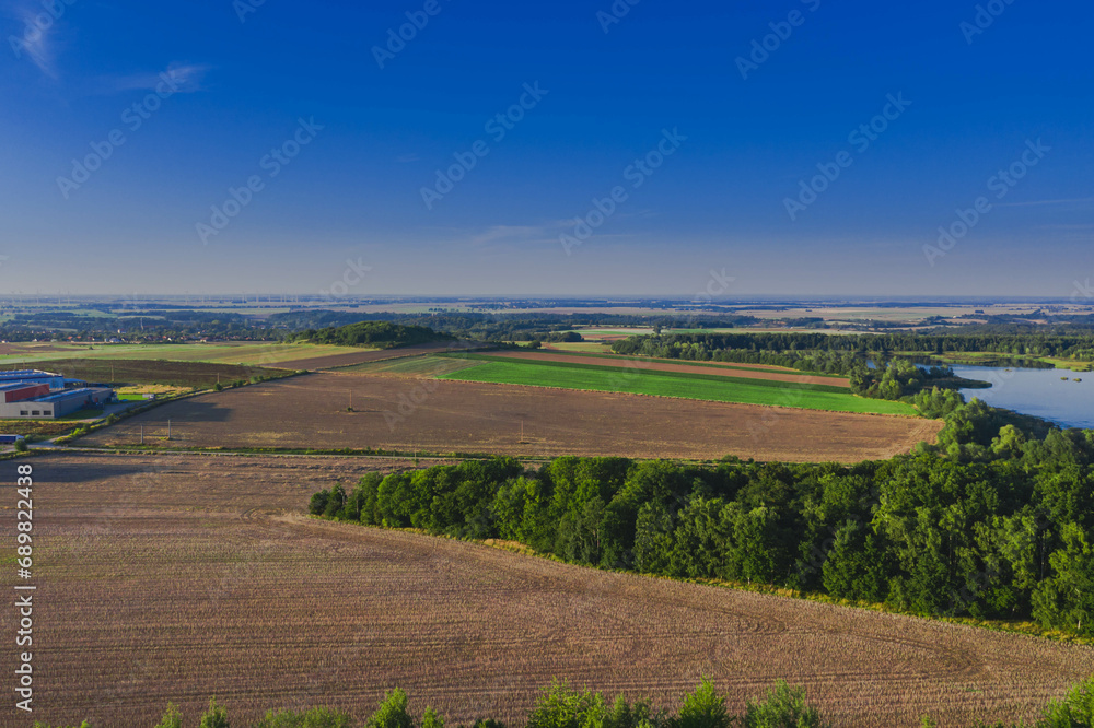 Rozległa równia pokryta porośniętymi trawą łąkami, lasami i brązowymi, zaoranymi polami uprawnymi. Zdjęcie wykonano z użyciem drona.