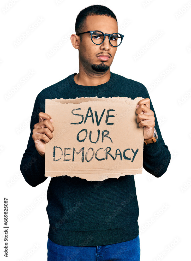 Young african american man holding save our democracy protest banner in shock face, looking skeptical and sarcastic, surprised with open mouth Young african american man holding save our democracy protest banner in shock face, looking skeptical and sarcastic, surprised with open mouth