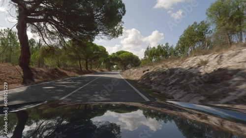 First person view, FPV, from dashcam of car driving along the Alentejo Coast in Portugal, passing cork oak trees and sand dunes. Road trip video in POV, with blue sky and clouds photo