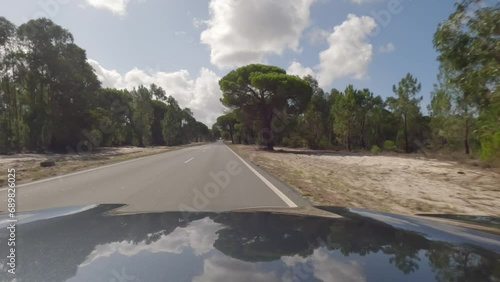 First person view, FPV, from dashcam of car driving along the Alentejo Coast in Portugal, passing cork oak trees and sand dunes. Road trip video in POV, with blue sky and clouds photo