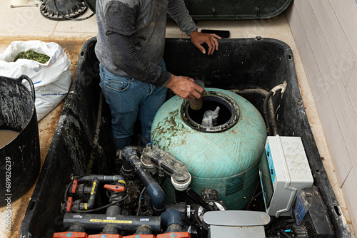 Hombre cambiando la arena del filtro de la depuradora de una piscina.	 photo