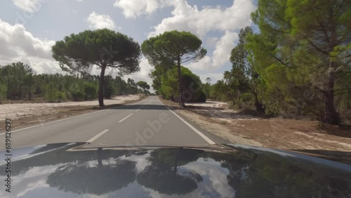 First person view, FPV, from dashcam of car driving along the Alentejo Coast in Portugal, passing cork oak trees and sand dunes. Road trip video in POV, with blue sky and clouds photo