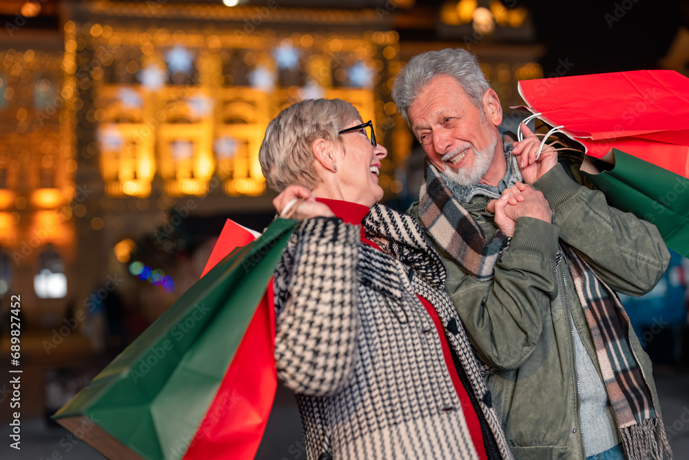 Senior couple in warm clothing walking outdoors with gift bags at night. Senior couple in warm clothing walking outdoors with gift bags at night.