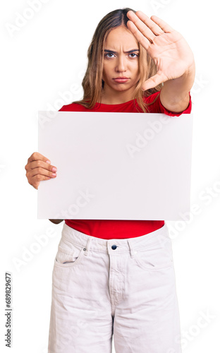 Young beautiful blonde woman holding blank empty banner with open hand doing stop sign with serious and confident expression, defense gesture photo