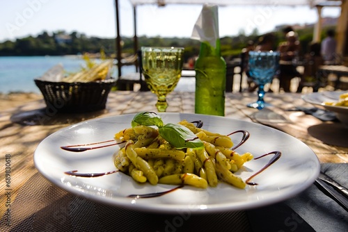 A plate of penne pasta on Sardinia, adorned with pesto, drizzled with balsamic vinegar, and garnished with fresh basil leaves. photo
