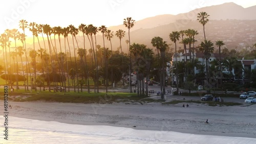 Drone flying over Pacific Ocean waves washing Santa Barbara beach, California, USA. City landmark in the sunset light. Panoramic landscape of streets and luxury houses of resort city, 4k footage 